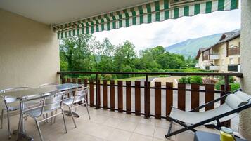 Ein Balkon mit einem Metalltisch und Stühlen, einem gepolsterten Stuhl und Blick auf Grünflächen und Gebäude im Hintergrund.