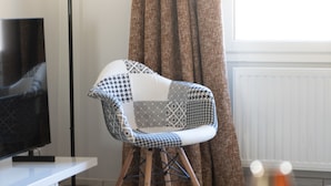 Una sala de estar moderna con un sillón estampado, un televisor de pantalla plana y una ventana con cortinas.