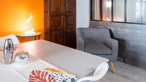 Una habitación moderna con una mesa blanca, un sillón gris, una puerta de madera y una ventana con vistas.