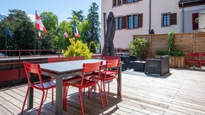 A wooden deck with a table and chairs, flags, and potted plants. - HIMALAYA, Annecy Rent Lodge (Annecy)