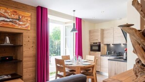 A modern kitchen with wooden cabinets, a dining table set for four, and a large window with pink curtains.
