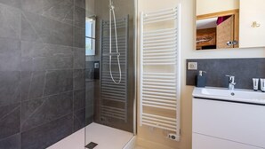 A modern bathroom with a glass-enclosed shower, a white towel rack, and a sink with a mirror above it.