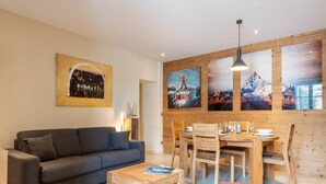 A modern living room with a sofa, coffee table, wooden dining table, and chairs. There are paintings on the wall and a wooden wall paneling. - APPENNINS, Annecy Rent Lodge (Annecy)