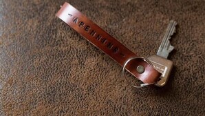 A key with a leather strap and metal ring, lying on a textured surface. - APPENNINS, Annecy Rent Lodge (Annecy)