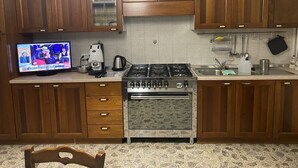 A kitchen with wooden cabinets, a gas stove, a coffee maker, and a television displaying a show.
