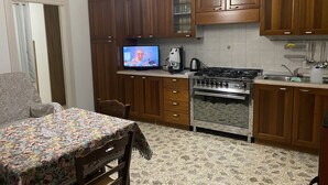A kitchen with wooden cabinets, a gas stove, a coffee maker, and a television displaying a news program.