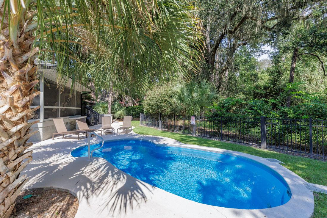 A swimming pool with a curved edge, surrounded by a fence and lush greenery.