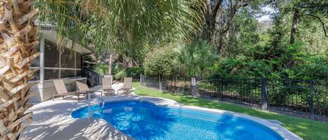 A swimming pool with a curved edge, surrounded by a fence and lush greenery.