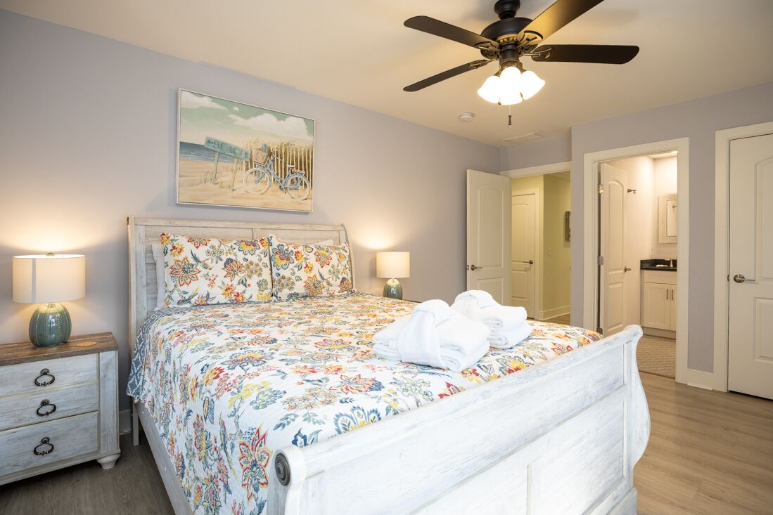 A bedroom with a bed, nightstands, a ceiling fan, and a painting on the wall.