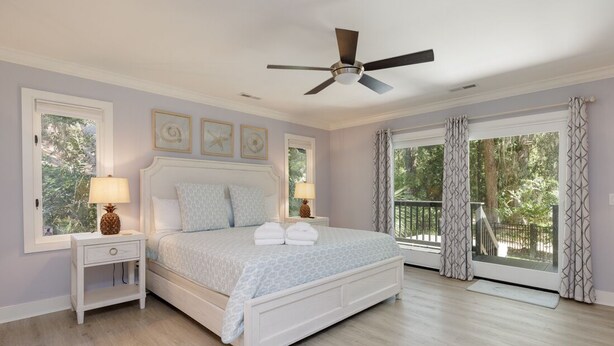 A bedroom with a bed, nightstands, a ceiling fan, and large windows with curtains. - 23 Willow Oak West: Sea Pines Home, 4BR, Pool, Hot Tub, Free Bikes (Hilton Head Island)