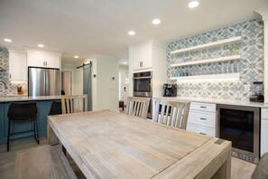 A modern kitchen with white cabinets, stainless steel appliances, and a wooden dining table.