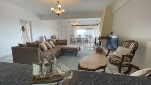 Ein Wohnzimmer mit einer Eckcouch, einem Couchtisch, einem Schiffsmodell, einem Essbereich mit Tisch und Stühlen sowie einer Chandelier.