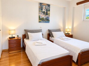 Habitación de hotel con dos camas individuales, cabeceros de madera, ropa de cama blanca, mesitas de noche con lámparas, una pequeña planta en maceta y un cuadro en la pared.