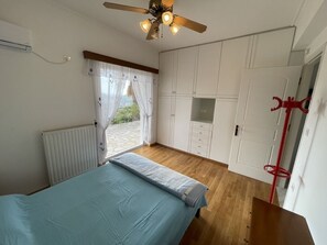 Une chambre à coucher comprenant un lit, un ventilateur de plafond, un radiateur, une fenêtre avec des rideaux et une armoire.