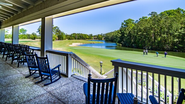 A covered outdoor seating area with chairs and a view of a golf course.