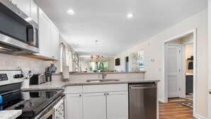 A modern kitchen with white cabinets, stainless steel appliances, a granite countertop, and a wooden floor.