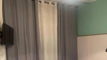 Un dormitorio con cama, cortinas, televisor montado en la pared y mesita de noche.