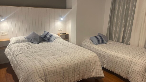 Habitación con dos camas, cada una con colcha y almohadas a cuadros. Se observan mesitas de noche con lámparas y un enchufe.