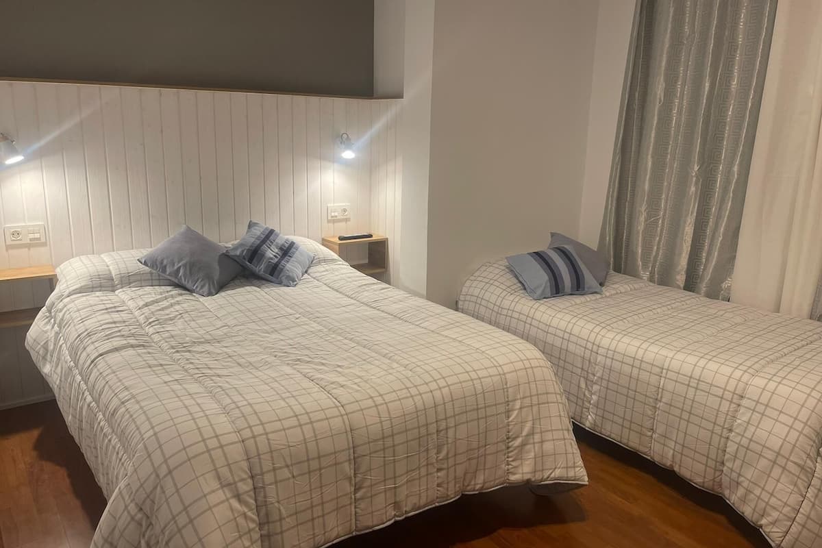 Een kamer met twee bedden, elk voorzien van een geruite plaid en kussens. Er staan nachtkastjes met lampen en een stopcontact.