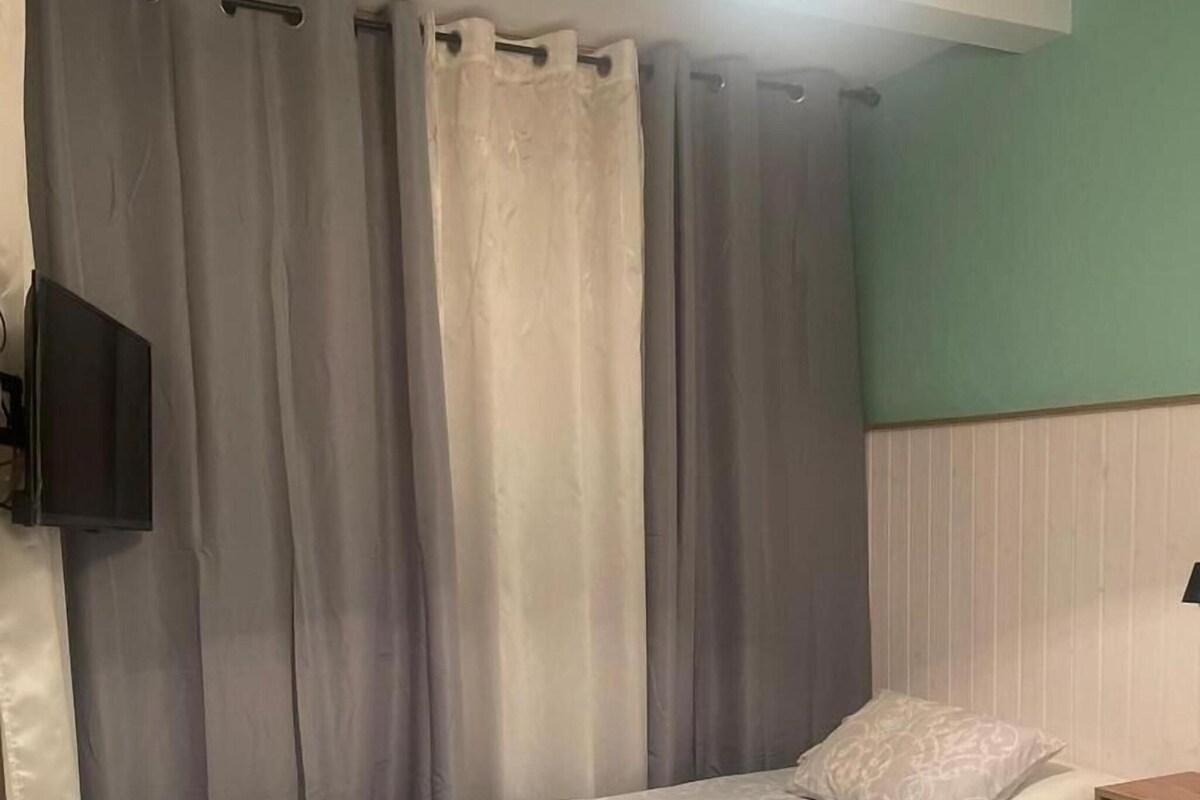 Een slaapkamer met een bed, gordijnen, een televisie en een nachtkastje.