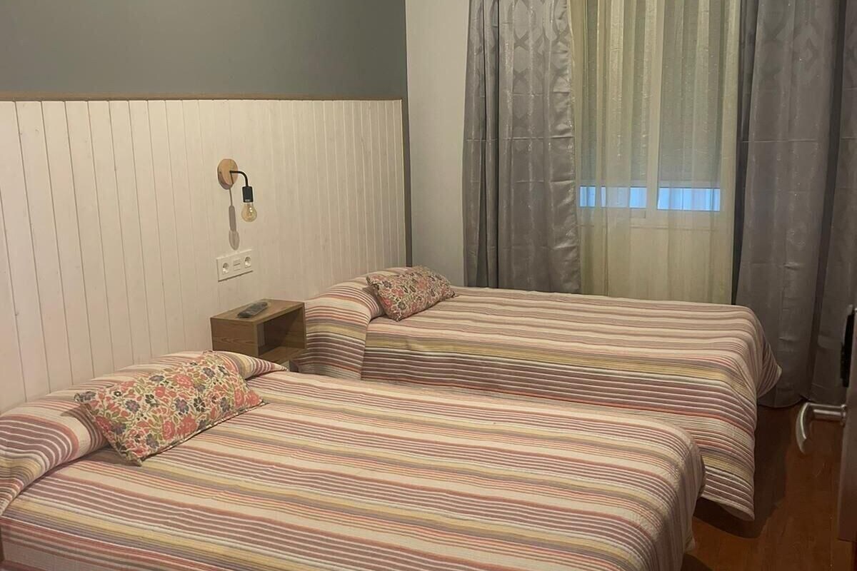 Een kamer met twee bedden, een nachtkastje, een lamp en een raam met gordijnen.