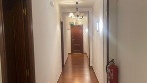 Un pasillo con suelo de madera, un candelabro y un extintor en la pared.