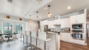Cozinha moderna com armários brancos, eletrodomésticos de aço inoxidável e um espaço bar com banquetas.