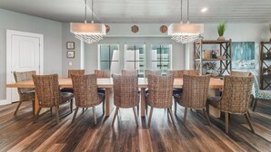 Uma sala de jantar com uma mesa de madeira comprida e cadeiras de vime, um candelabro e uma estante com objetos decorativos.