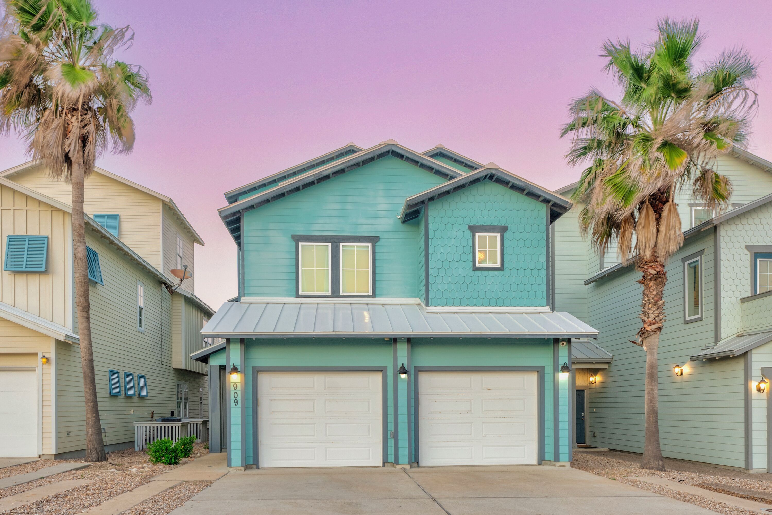 A two-story house with a garage, a porch, and palm trees.