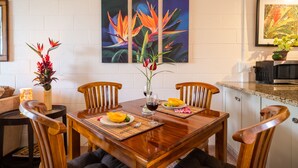 A dining area with a wooden table, four chairs, and a vase with flowers. There are two paintings on the wall above the table.