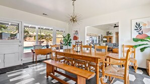A dining area with a wooden table and chairs, a bench, and a view of a vineyard through large windows.