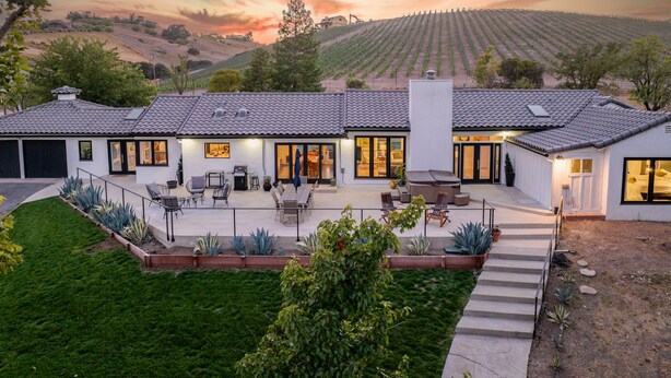 A modern house with a patio, large windows, and a view of vineyards.