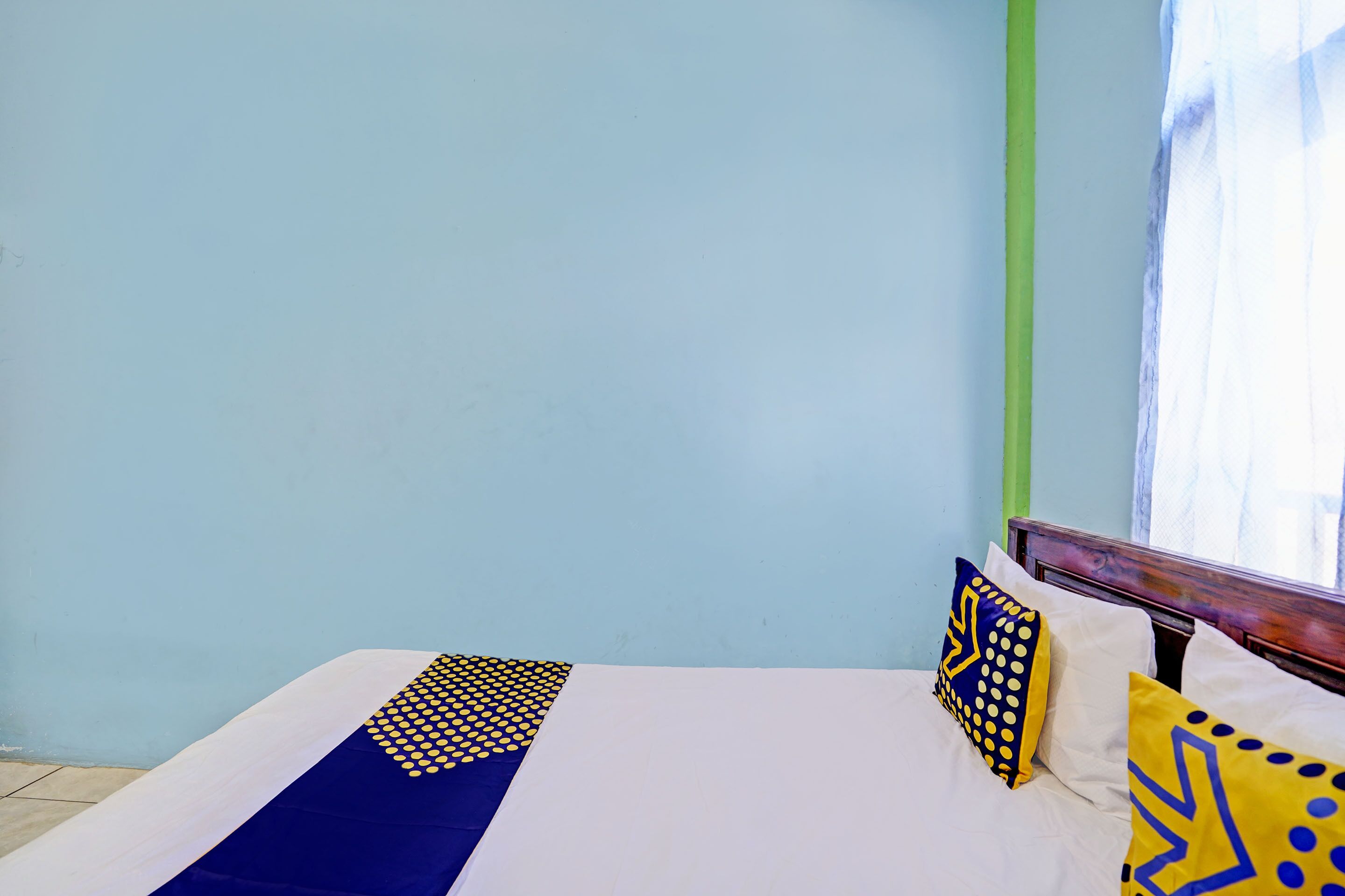 Una cama con colcha azul y blanca, dos almohadas con diseños azules y amarillos, y un cabecero de madera.