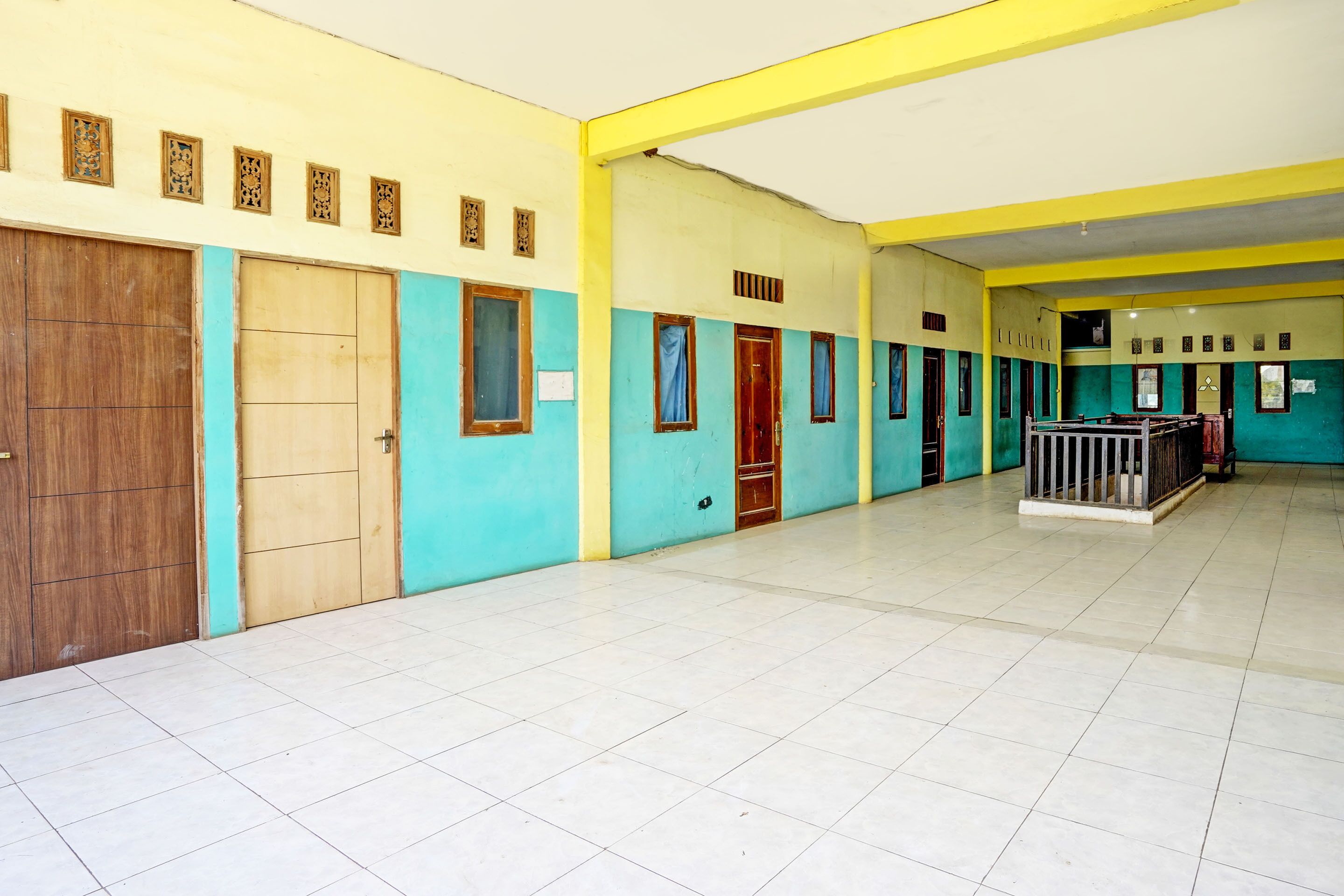 A spacious corridor with tiled floors, wooden doors, and blue-framed windows.