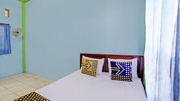 Ein Schlafzimmer mit einem Bett, zwei Kissen mit geometrischen Mustern, einem blauen Vorhang und einem kleinen Fenster, an dem ein Handtuch hängt.