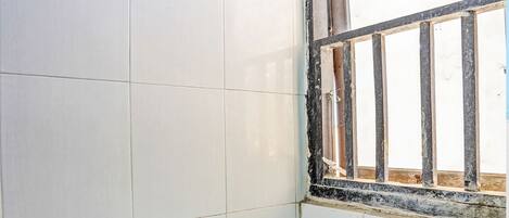 A small bathroom with a blue toilet, white and blue patterned tiles, and a window with metal bars.
