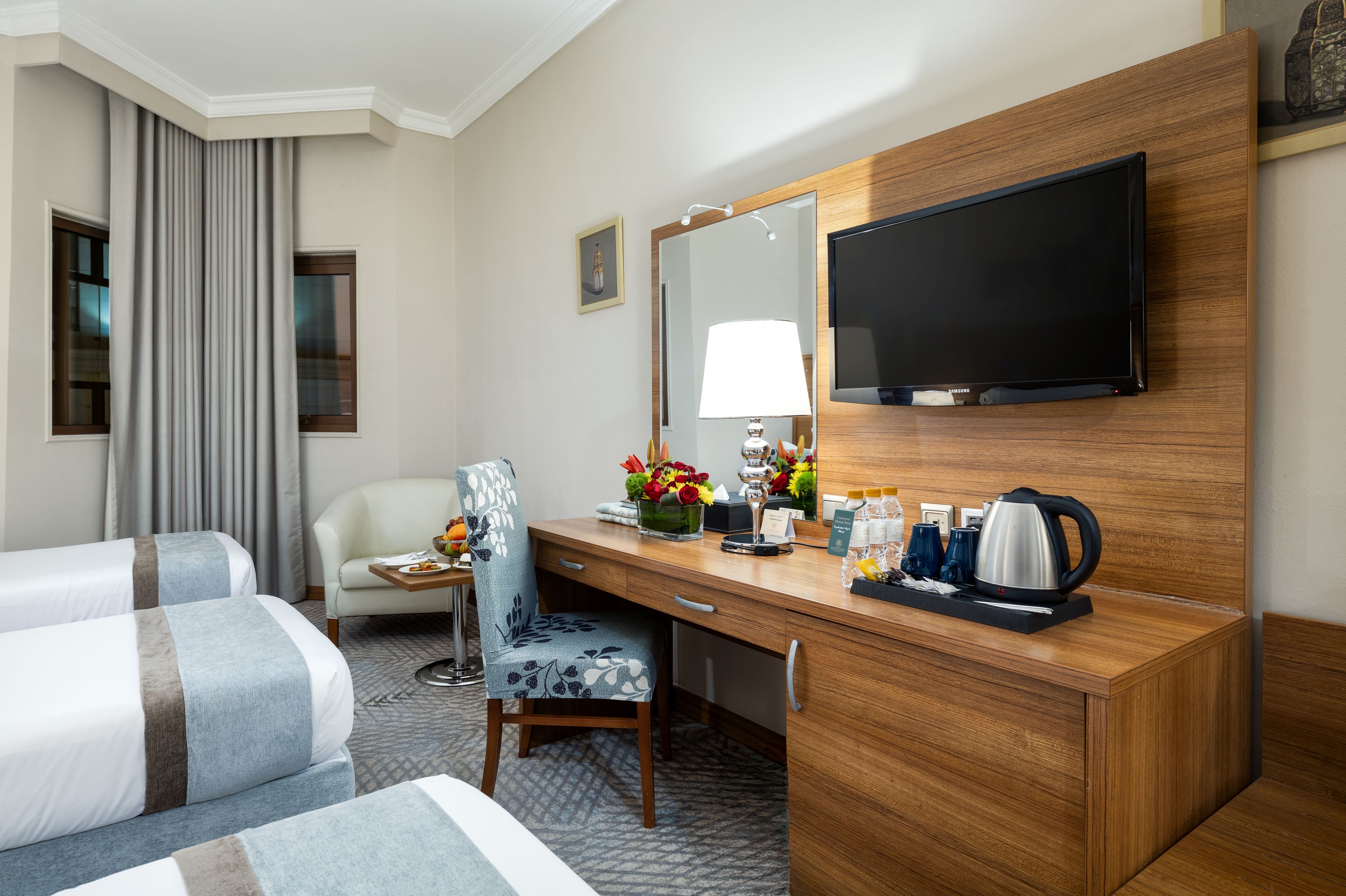 A hotel room with a bed, a desk with a lamp, a chair, a television, and a coffee maker.