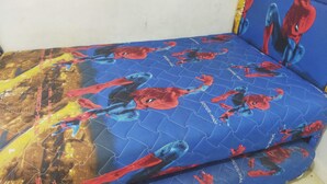 A bed with a blue mattress featuring Spider-Man prints.