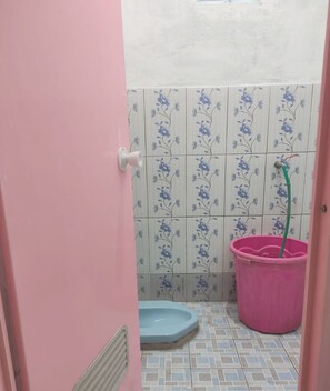Un baño con una puerta rosa, un inodoro azul, un cubo rosa y baldosas con estampado floral.
