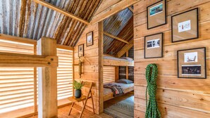 A rustic wooden cabin interior with a bunk bed, framed pictures on the walls, a small table with a plant, and a rope hanging on the wall. - 6 Person Cabin, Surrounded by Nature in Tintagel (Tintagel)