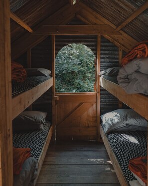 A narrow wooden cabin with bunk beds, a wooden door, and a window overlooking a forest. - 6 Person Cabin, Surrounded by Nature in Tintagel (Tintagel)