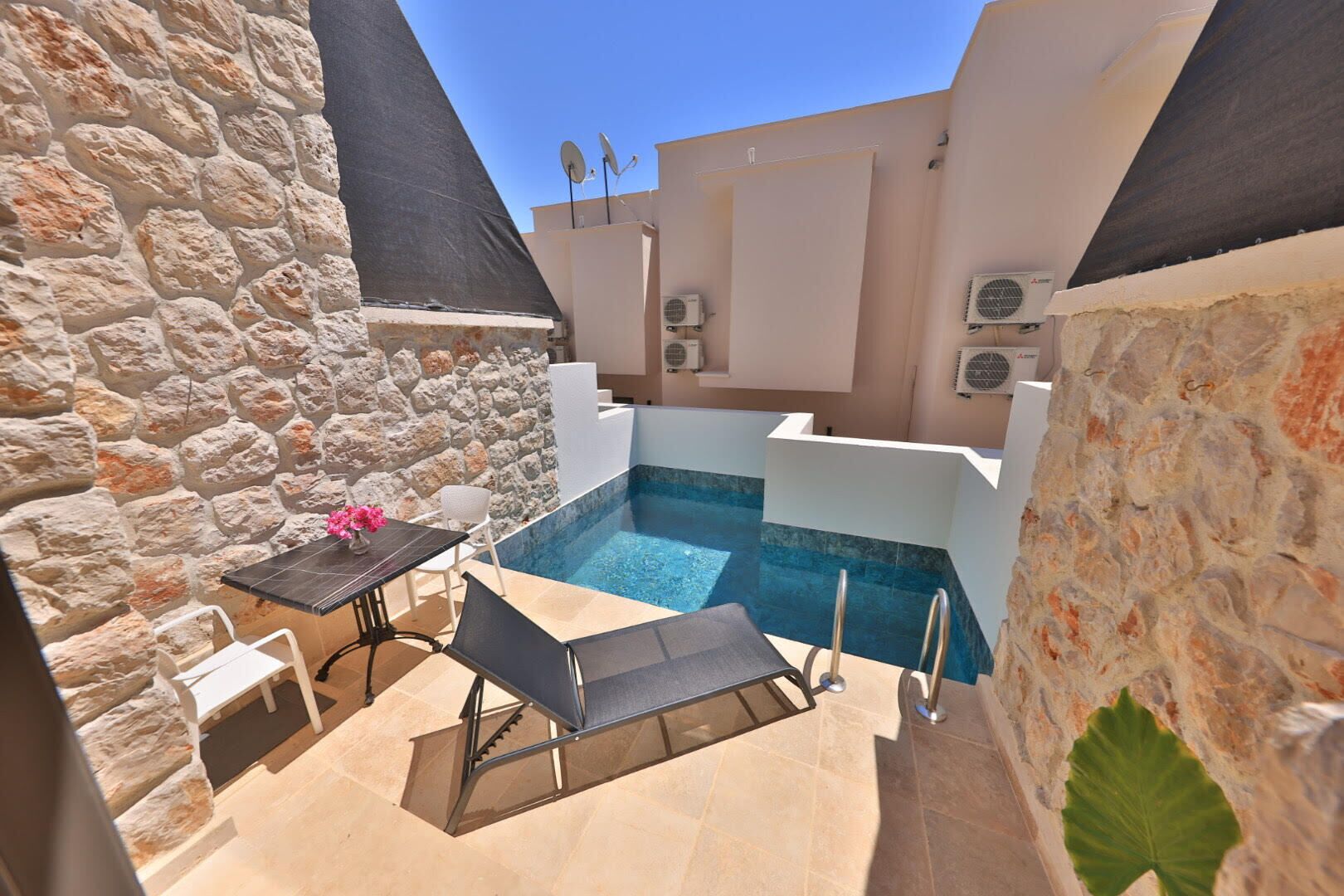 A small outdoor pool area with stone walls, a table with chairs, and a lounge chair.