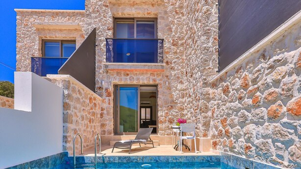 A stone building with a swimming pool, two lounge chairs, and a table with a chair. - Nouba Villas (Kas)