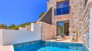 A stone building with a swimming pool, a lounge chair, and a small table with flowers. - Nouba Villas (Kas)