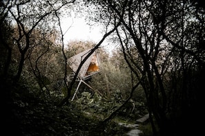 Una casa árbol aislada con techo inclinado, rodeada de un bosque denso.