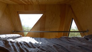 A tent-like room with a bed, a window, and a metal rod. - K4 Kudhva Treehouse Cabin With sea View (Tintagel)
