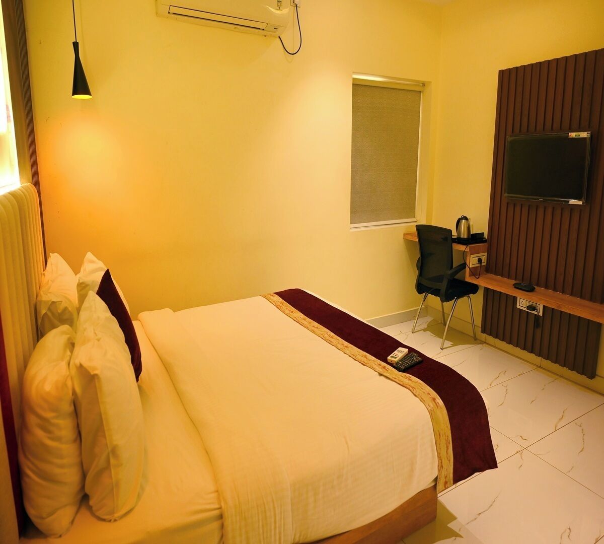 Habitación de hotel con cama, escritorio, silla, televisor y ventana.