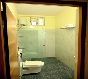 Uma casa de banho compacta com sanita, chuveiro com divisória de vidro e chão em mosaico de mármore.