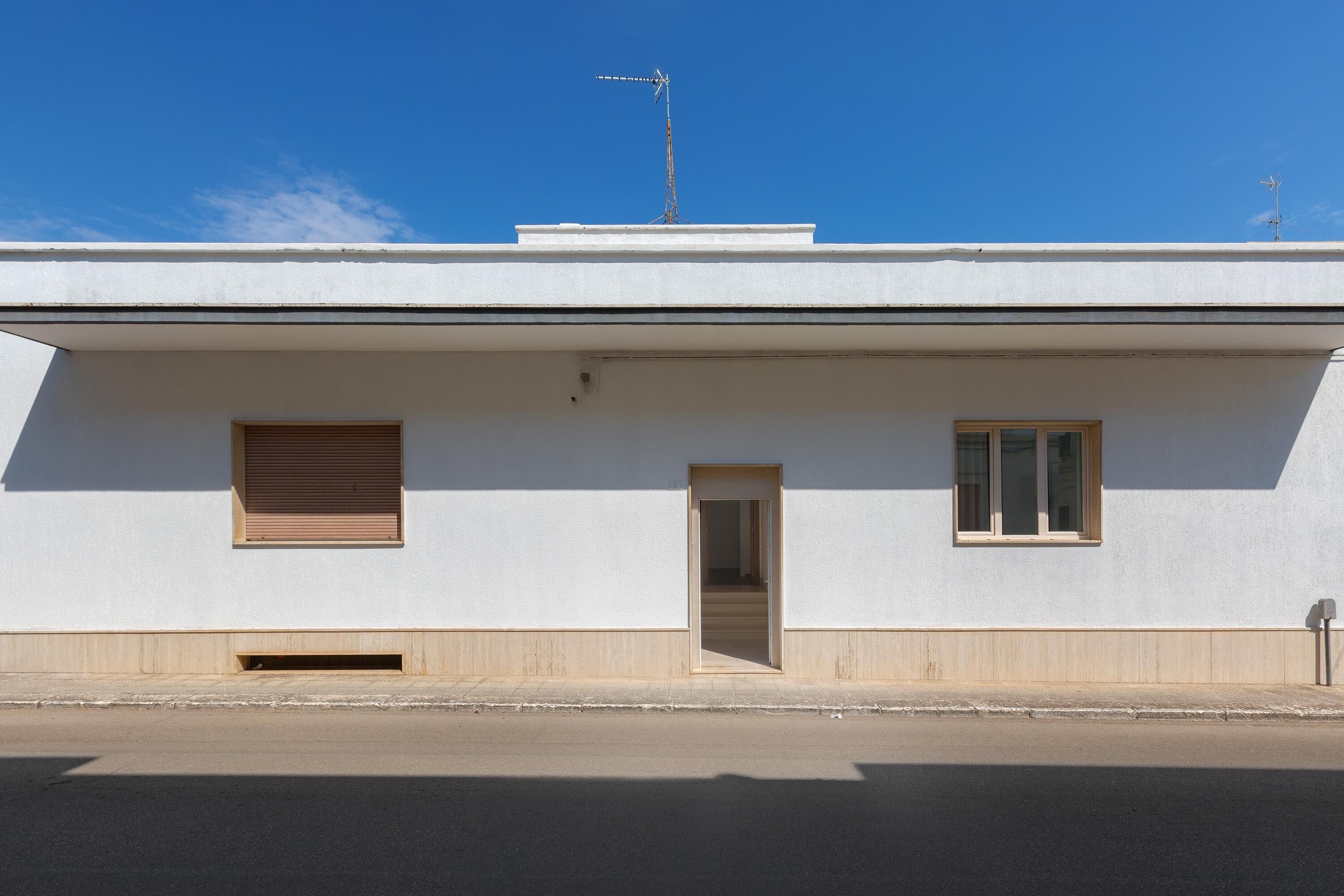 A modern building with a flat roof, a small entrance, and two windows.