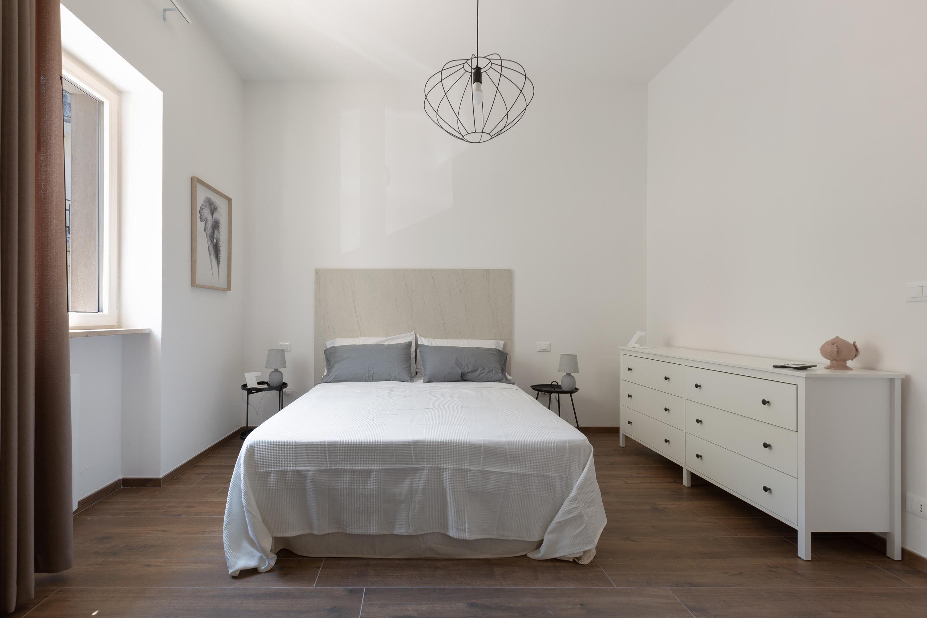 Une chambre à coucher avec un grand lit, des tables de chevet, une commode et un luminaire suspendu.